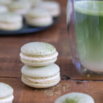 Two stacked matcha macarons next to a matcha latte.