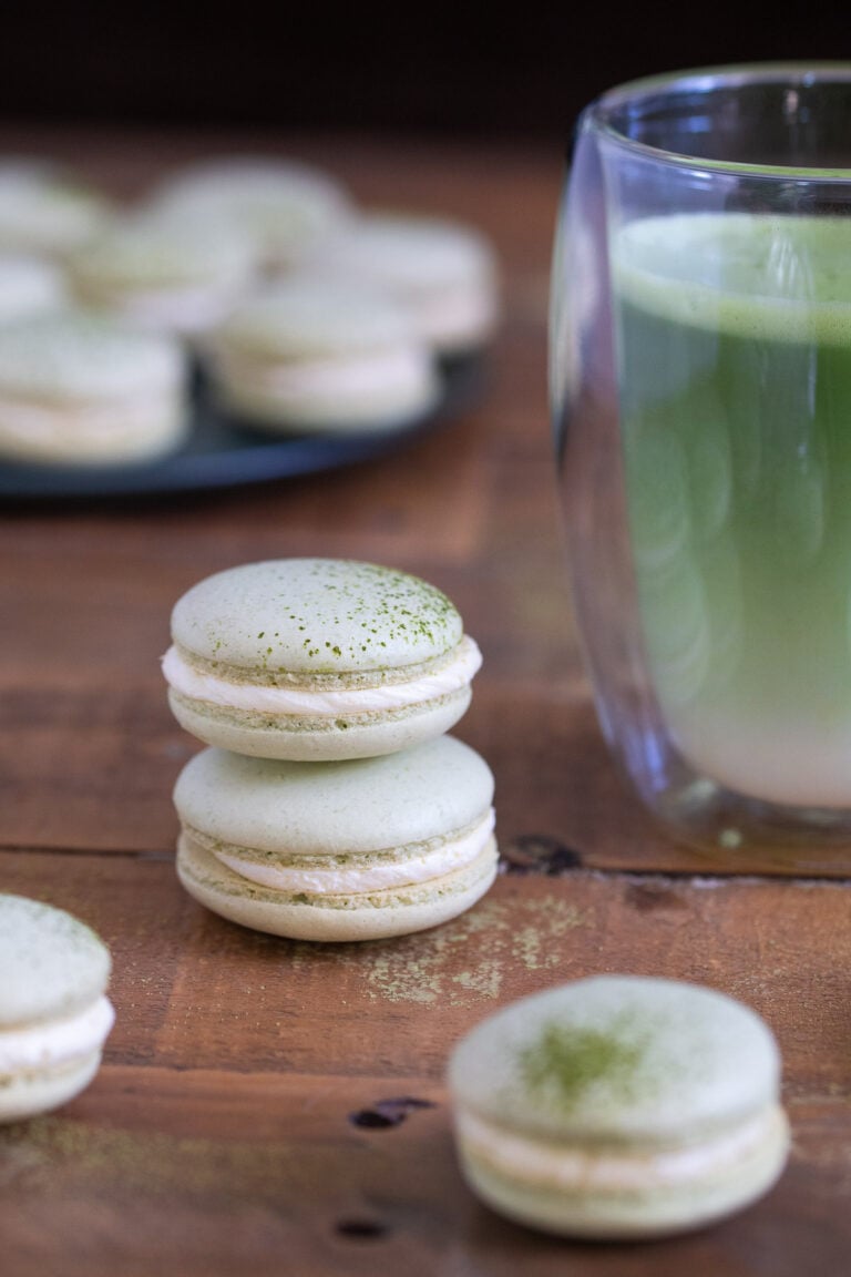Two stacked matcha macarons next to a matcha latte.
