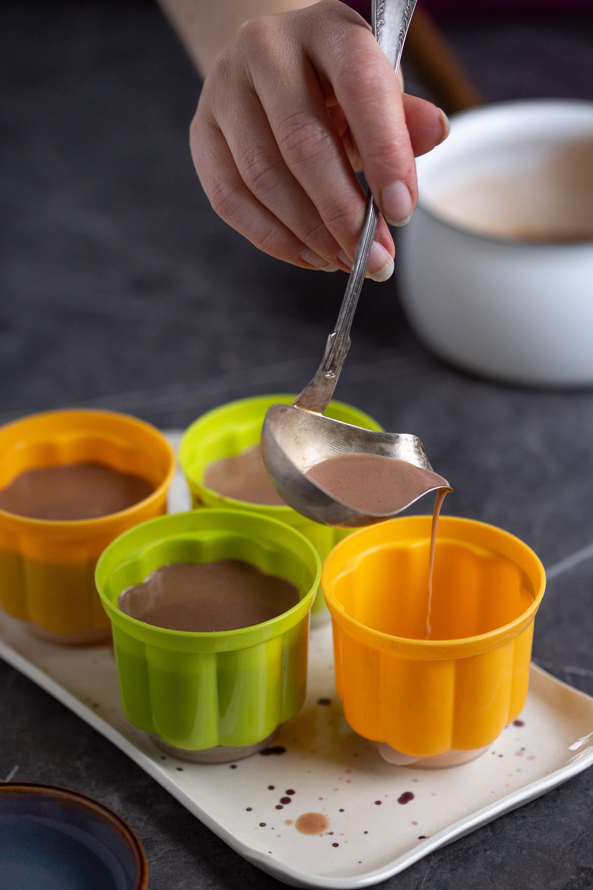 Hand pouring panna cotta into moulds.