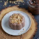 Nutella panna cotta topped with chopped hazelnuts, served on a small white plate.