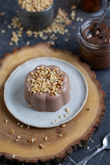 Nutella panna cotta topped with chopped hazelnuts, served on a small white plate.