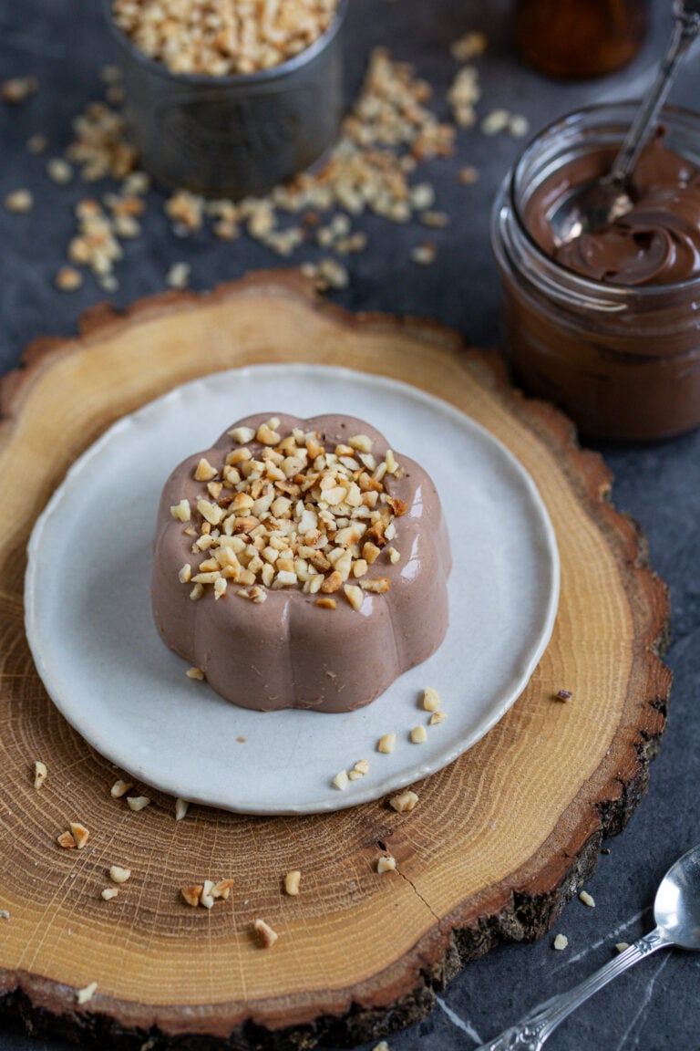 Nutella panna cotta topped with chopped hazelnuts, served on a small white plate.